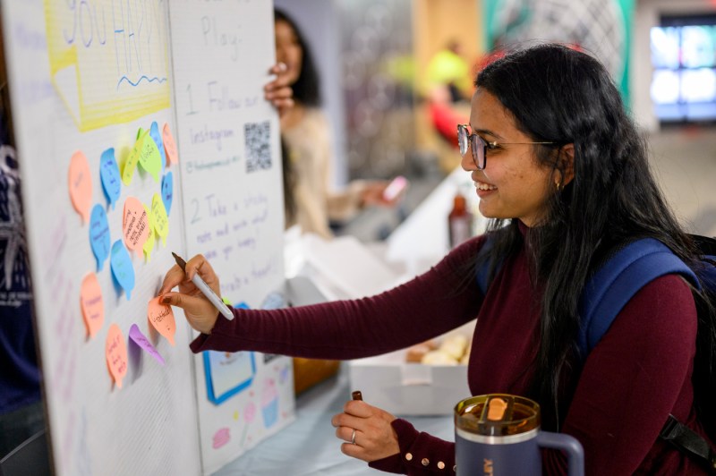A student writes responses on a poster during the Happiness Cup Club’s tabling event at Curry Crossroads.