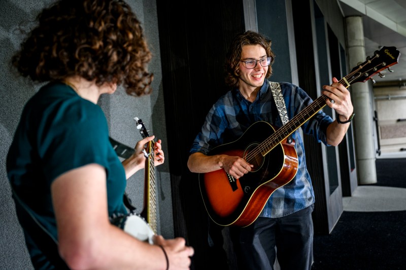 Two people stand on a stage. One plays the banjo while another plays a guitar.