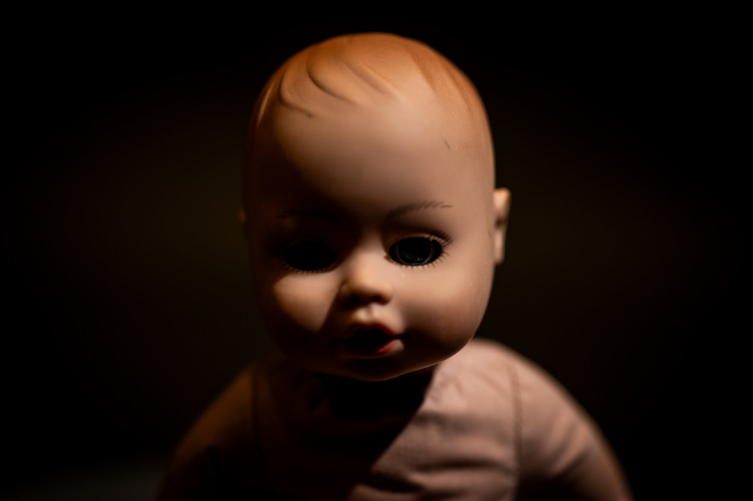 Close-up of a baby doll's face emerging from darkness, with one eye visible, creating an eerie atmosphere.