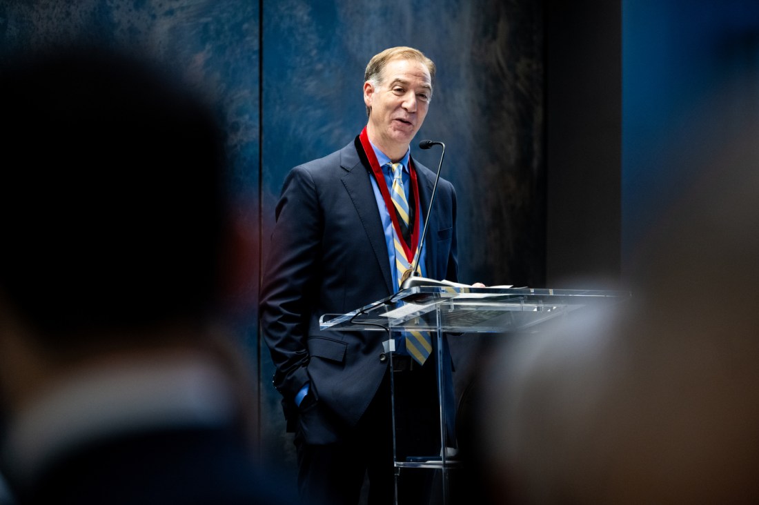 Charles Hillman, wearing a medallion, speaks at a podium.