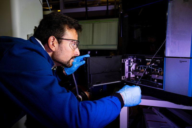 A professor, who is wearing safety glasses and gloves, uses a piece of lab equipment.