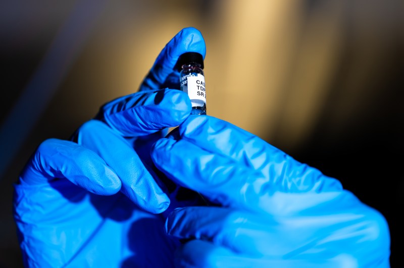 A close-up photo of a person's hands wearing gloves and holding up a test tube.