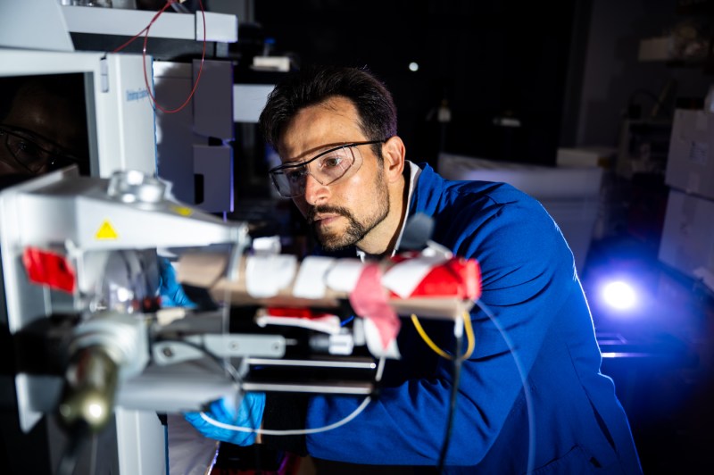 A person wearing safety glasses looks closely at a piece of lab equipment.