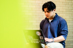 Northeastern student Rick Li shown seated in a blue shirt working on a laptop.