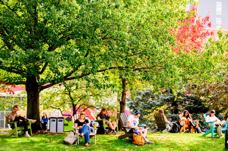 Students sit outside on Adirondack chairs on the Boston campus.