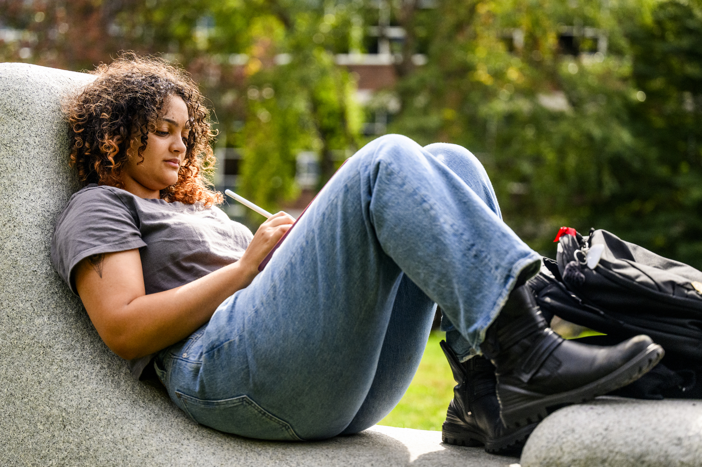 A student rests on a stone wall on the Boston campus.