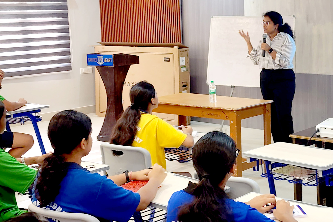 Anjali Laddha depicted presenting in front of a classroom.
