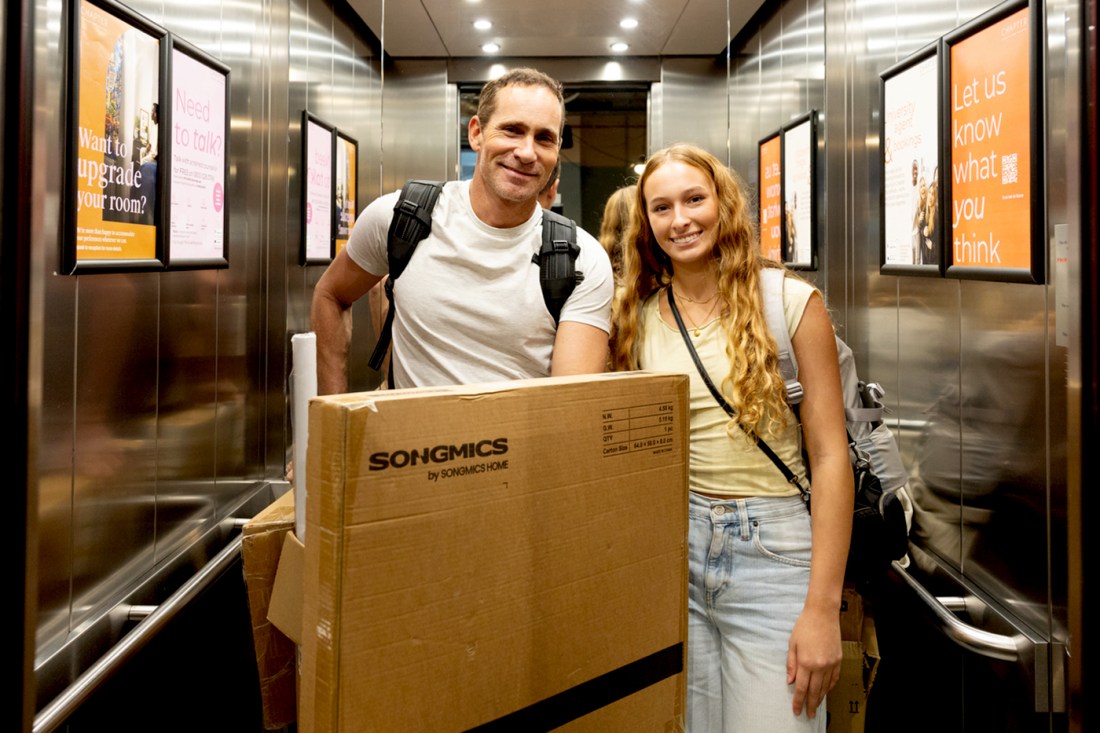Two people standing in an elevator behind a large cardboard box.