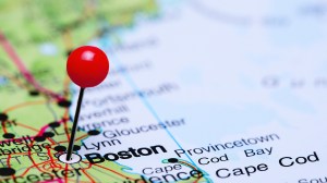 A closeup of a paper map with a pin in the city of Boston.