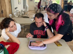 Three people sitting and standing around an iPad that is resting on a table.