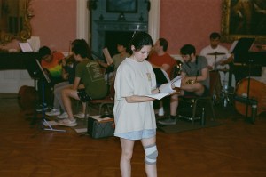 Brooke Di Spirito, a white woman, depicted reading a script with a knee brace and a white T-shirt.