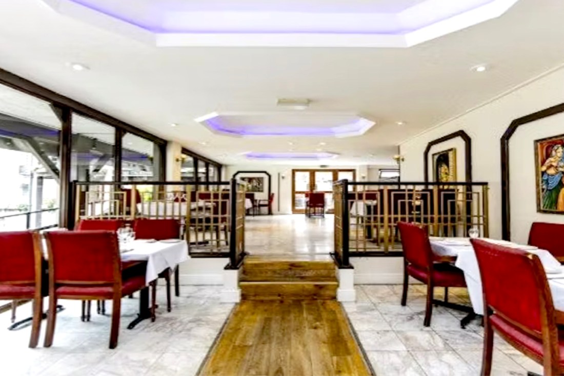 Interior of former Mala Indian restaurant at St Katherine Dock showing white marble floors, red upholstered chairs, ornate wooden dividers, and decorative wall art before conversion to office space.