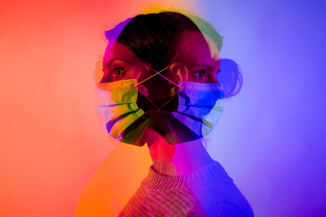 Person wearing a face mask in colorful rainbow lighting with red, orange, purple, and blue hues.