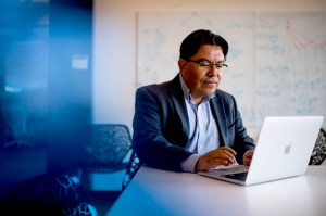 Mauricio Santillana shown sitting at a desk and typing on his laptop.