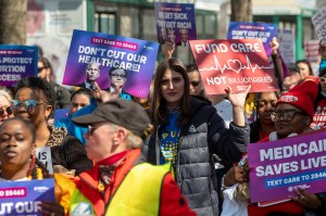 Protesters carrying purple signs displaying information about health care costs.