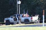 A far shot of law enforcement standing next to a vehicle used to ram a church building, which contains two American flags in its back portion.