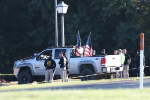 A far shot of law enforcement standing next to a vehicle used to ram a church building, which contains two American flags in its back portion.