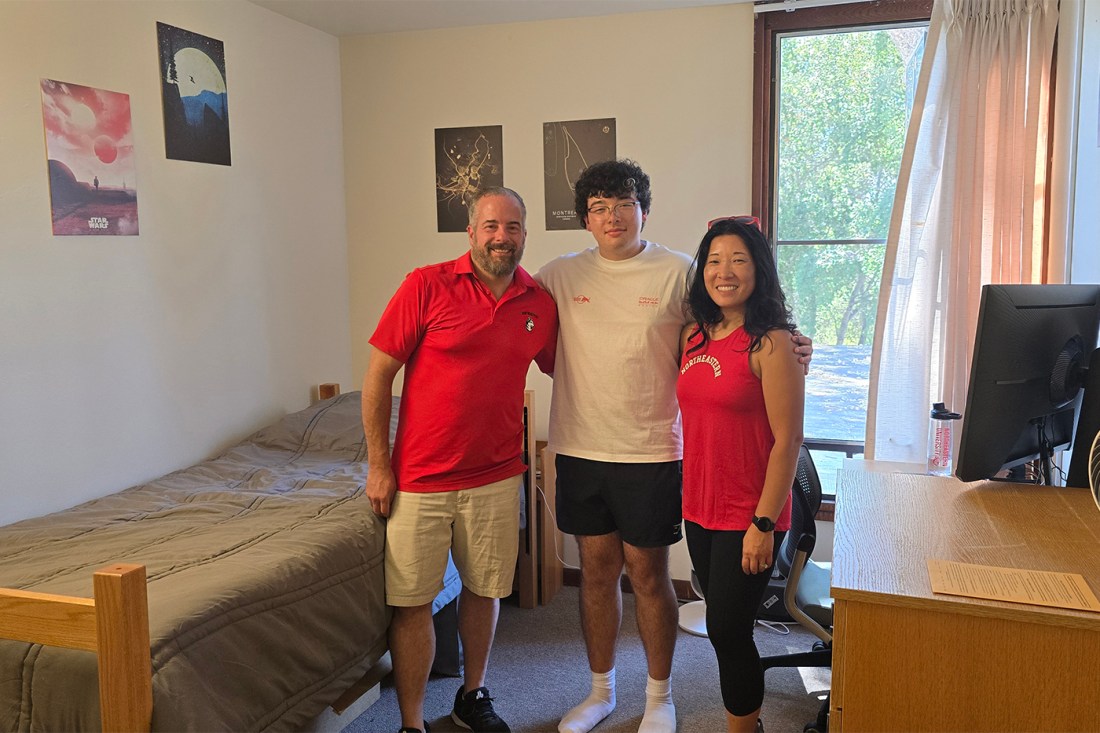 Sarah and Scott Pelletier posing with one of their sons in a dorm room.