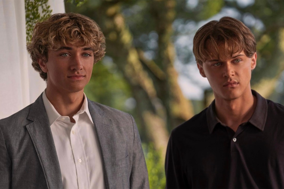 Two blonde male stars of "The Summer I Turned Pretty" standing next to one another against a leafy backdrop.