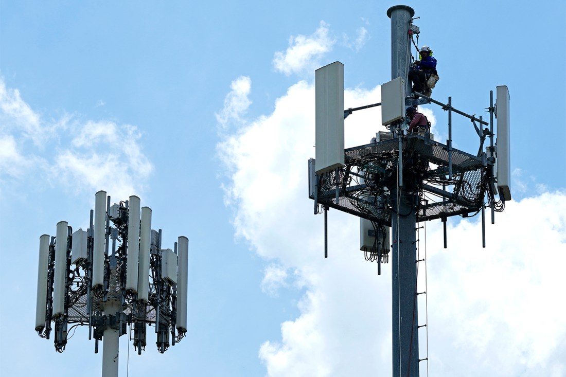 Workers depicted inside two adjacent cell towers against a blue sky.
