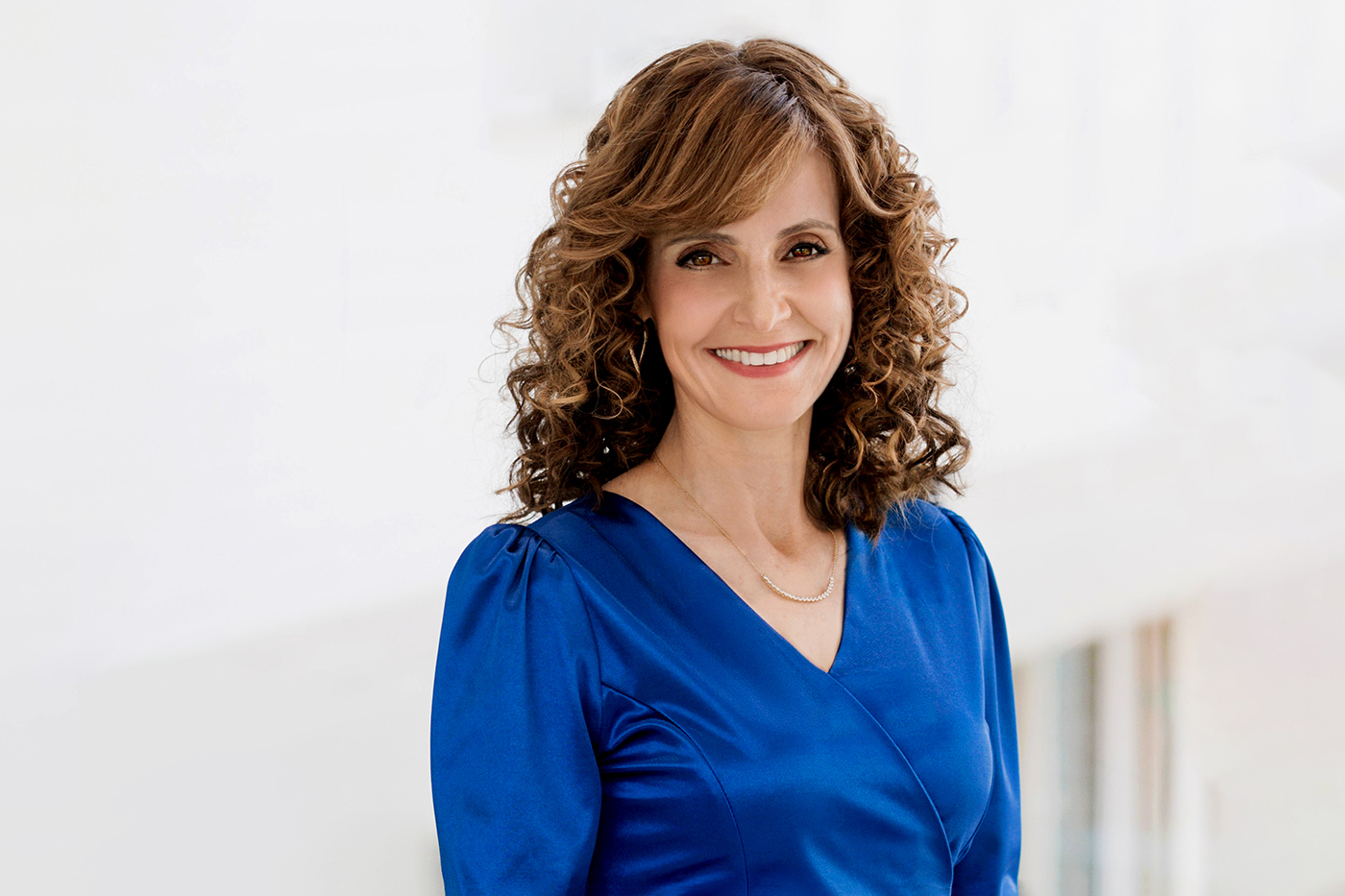 Yonina Eldar is wearing a blue dress and smiling against a bright white backdrop.