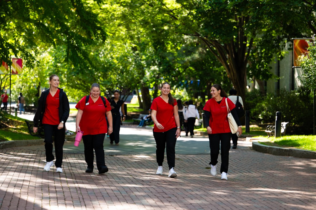 Four Northeastern nursing students in red scrubs walk together on campus.