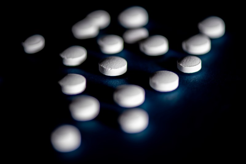 Small white medication tablets shown against a black backdrop.