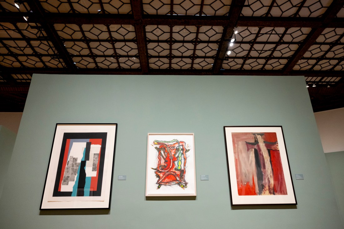 Three framed abstract artworks hung in a row on a blue-grey gallery wall. 