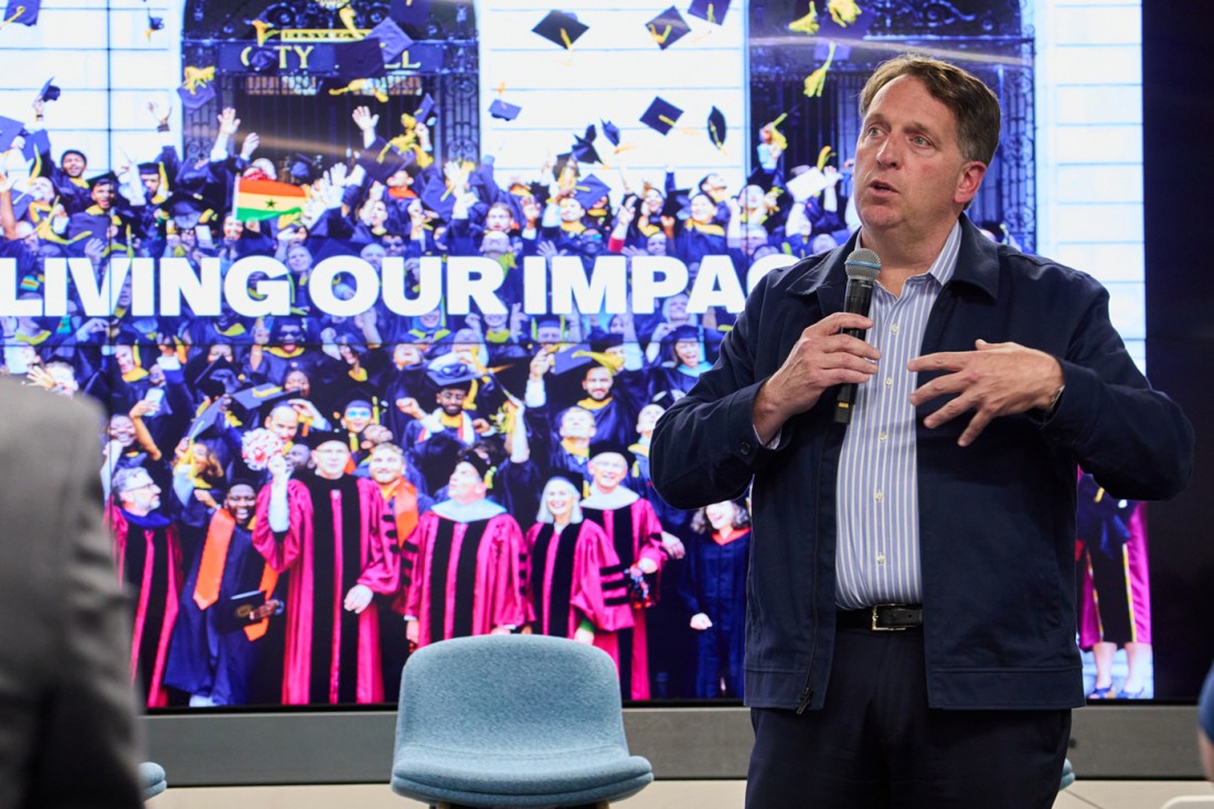 Speaker presents at Roux Institute event with graduation celebration image showing 'Living Our Impact' displayed on screen behind him.