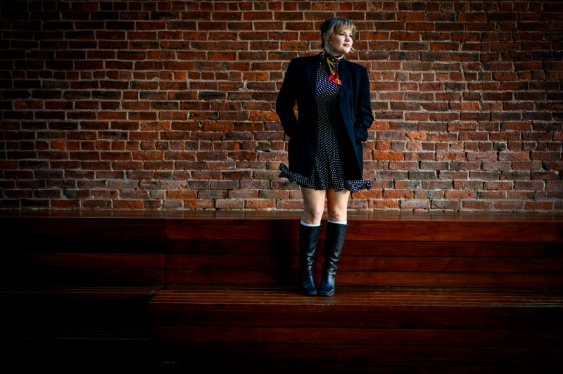 Haylen Wehr in a polka dots dress standing against a red brick wall.