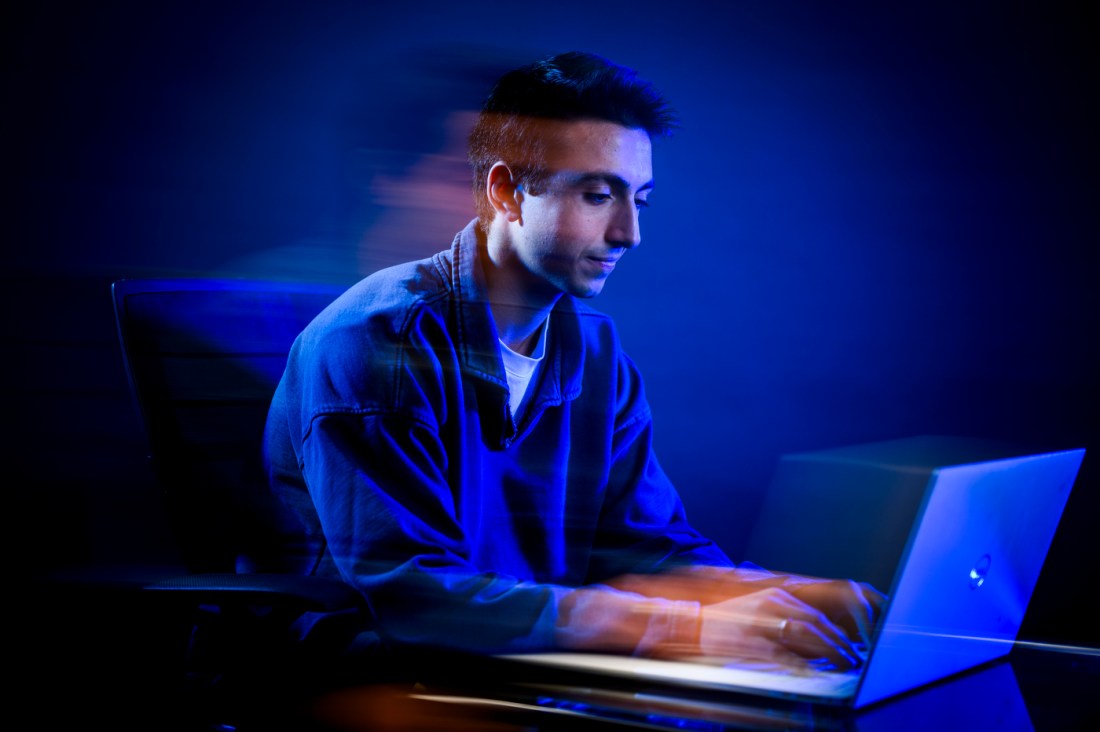 Ruben Noroian, a young man with dark hair, depicted seated in a collared shirt while he works on a laptop.
