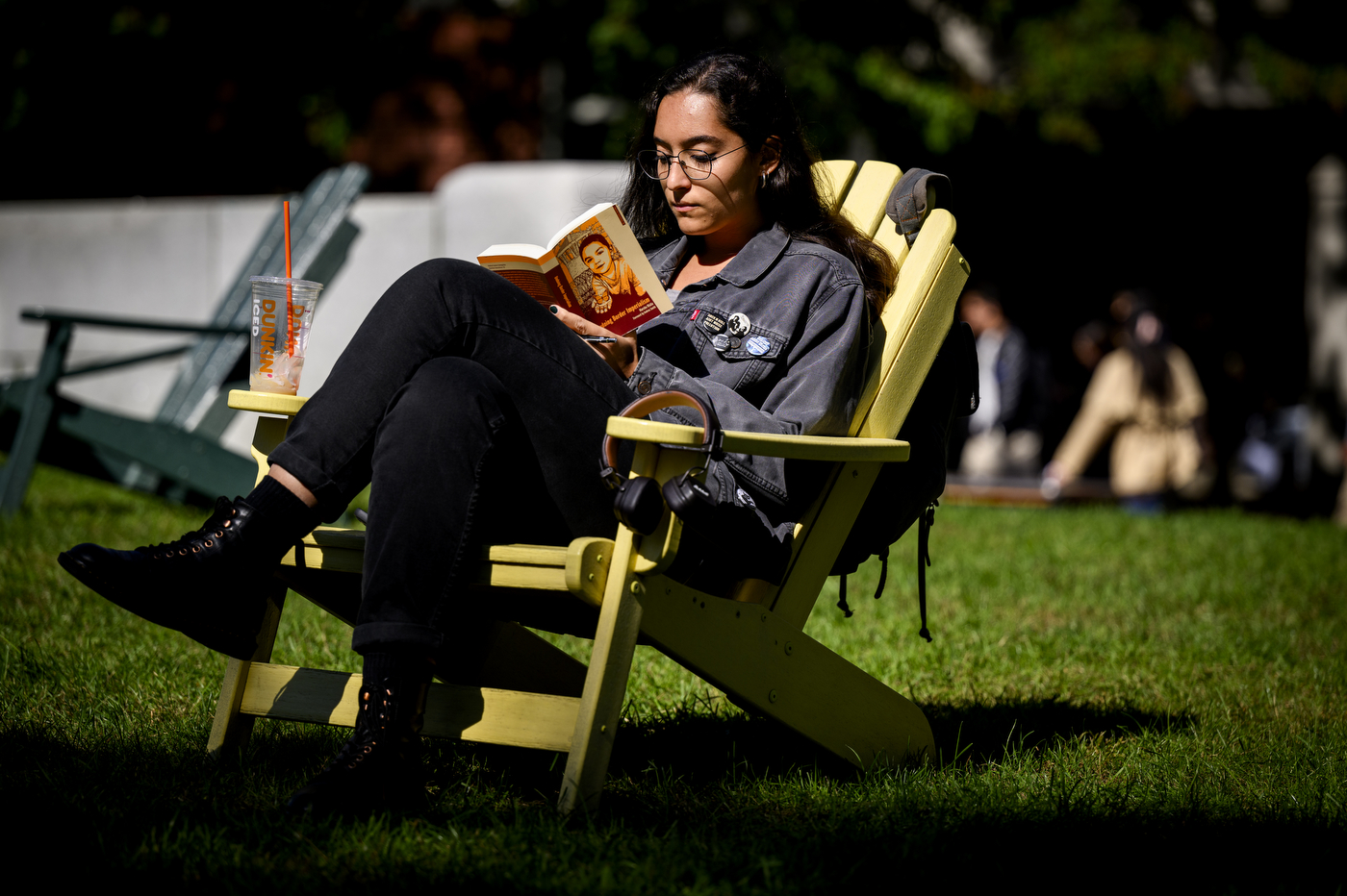 A student reads a book while sitting on an Adirondack chair.