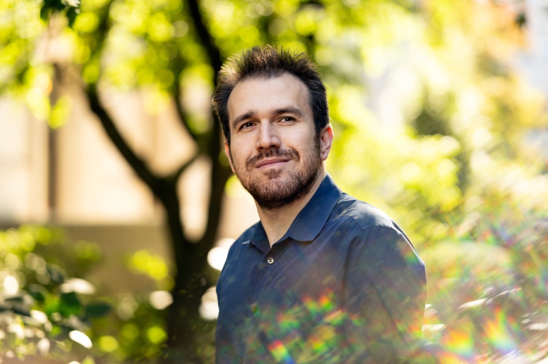 A portrait photo of Norair Khachatryan, smiling outside amongst greenery.