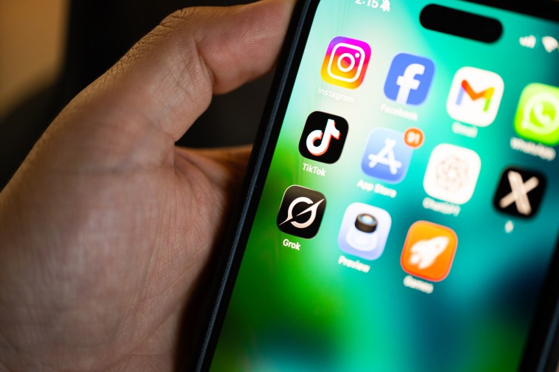 A hand holding an iPhone showing several apps on the home screen.