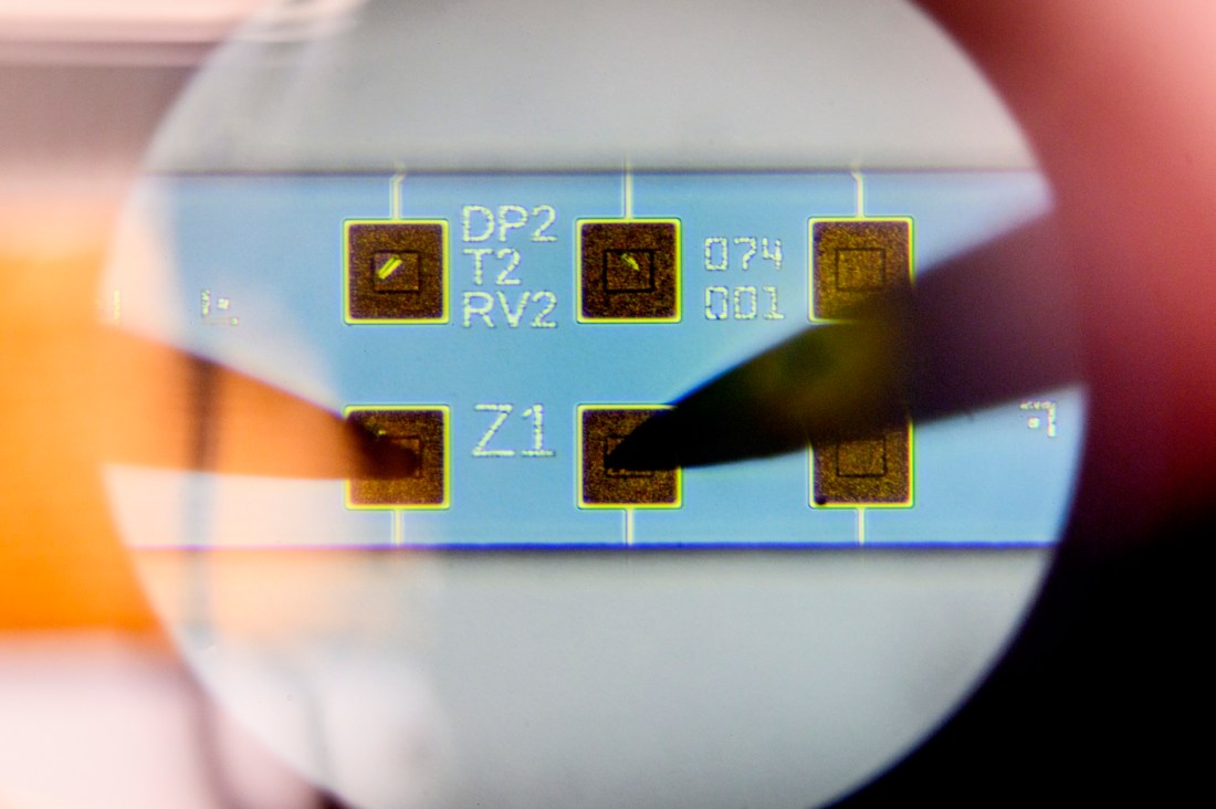A close-up of a microchip with gold contact points and labeled squares, viewed under magnification.