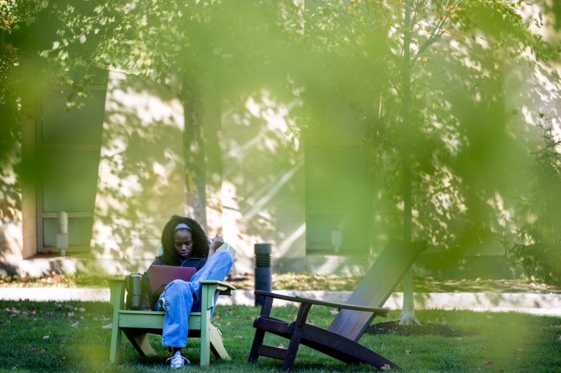 A person sits on an Adirondack chair outside.