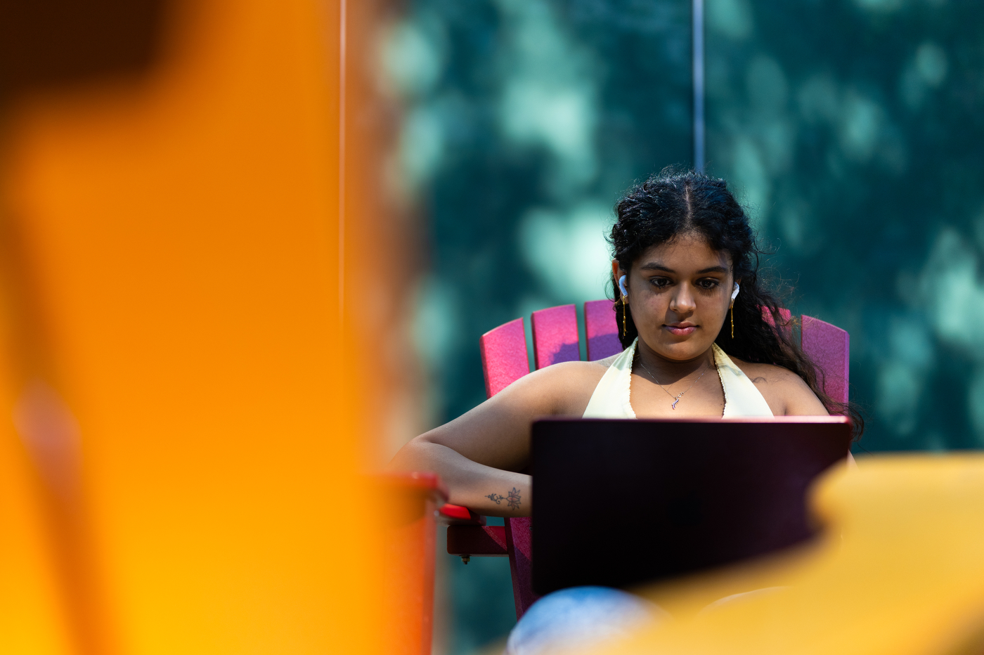 A student works on a laptop while sitting outside on an Adirondack chair.