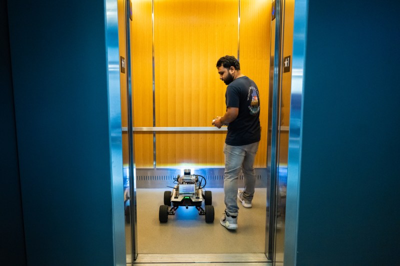 A student brings a robot onto an elevator. 