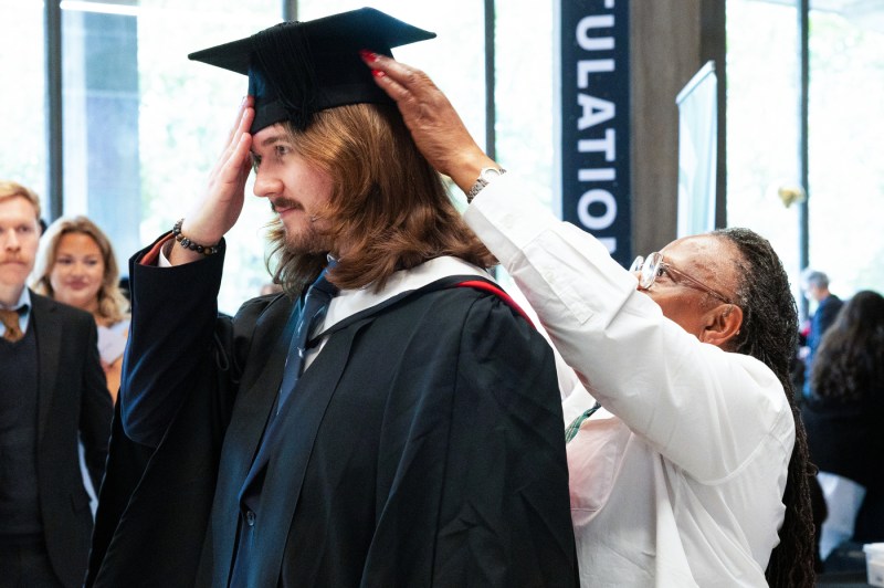 A student receives help securing their mortarboard for graduation.