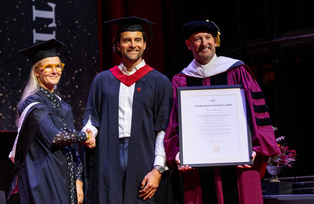 A graduate poses on stage with two faculty members during the London graduation ceremony at Queen Elizabeth Hall.