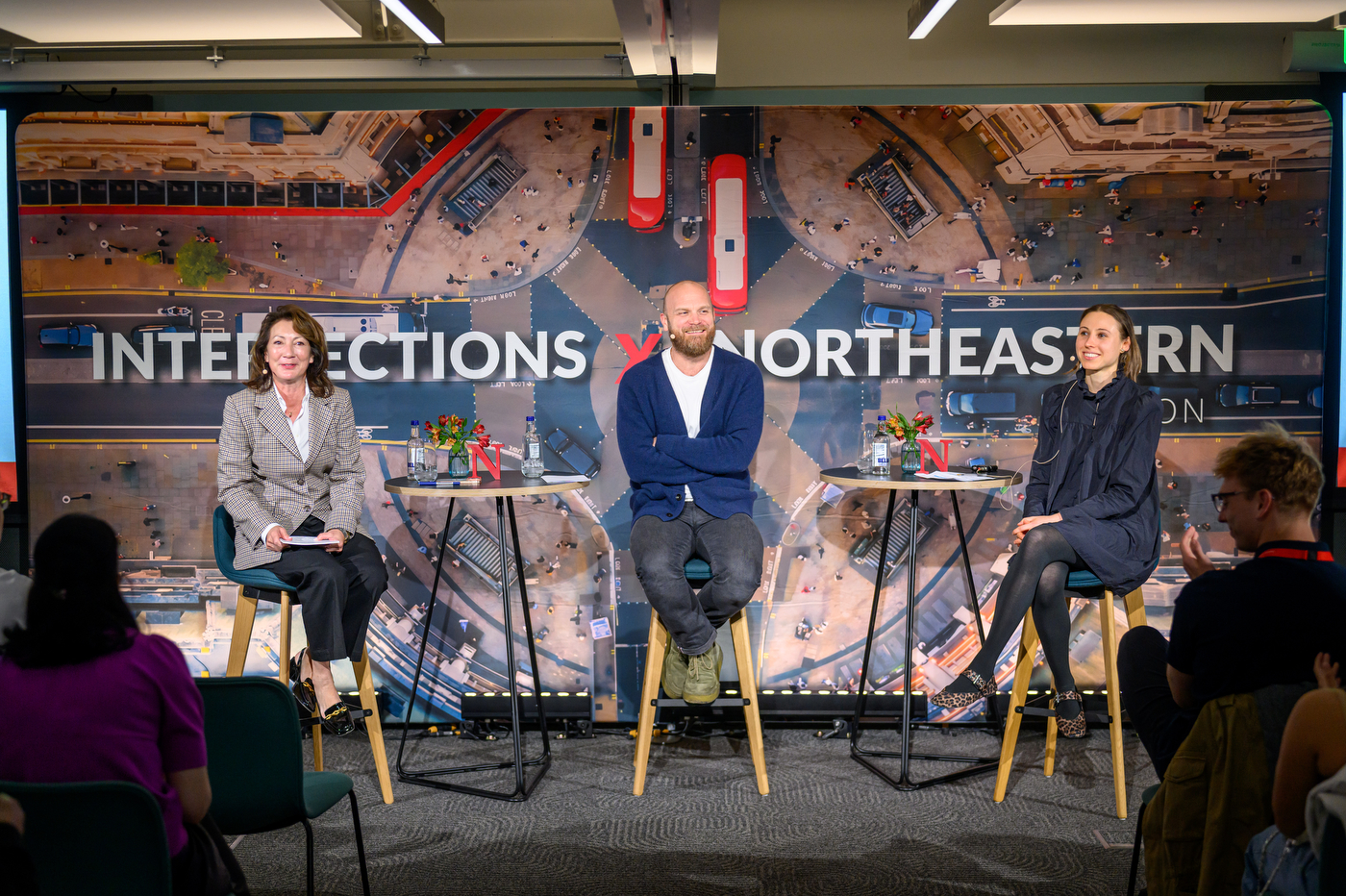 Will Champion posing for a photo on a panel stage next to two other people. 
