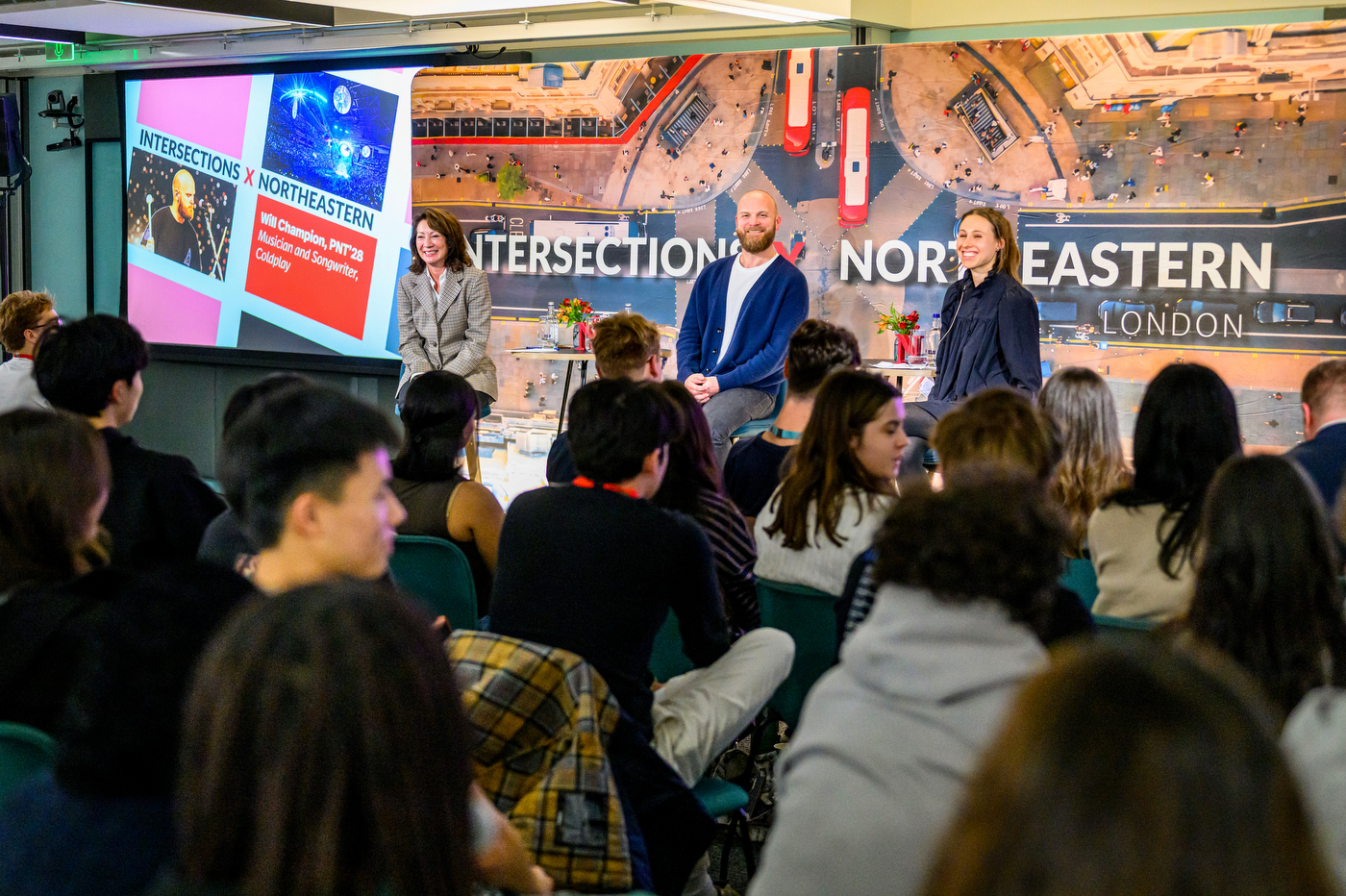 Will Champion and two other people smile on stage in front of a group audience. 