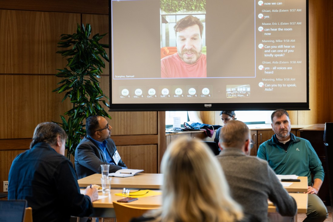A speaker appears on a video call projected on a large screen during the AI leadership panel at Northeastern’s Alumni Center.