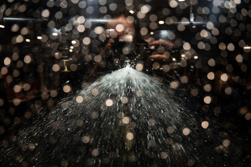 Water sprays dramatically from a central nozzle in a dark interactive display, creating a fountain-like effect with droplets suspended in mid-air. Circular bokeh lights dot the foreground. 