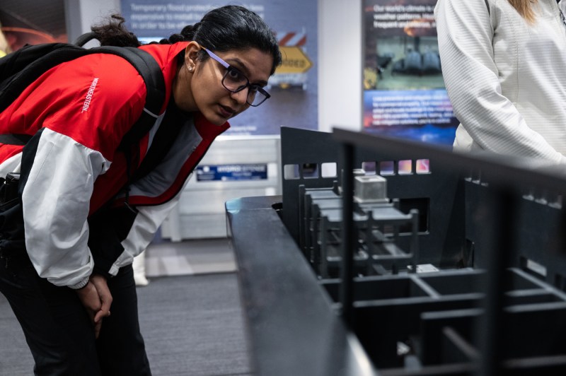 A person wearing glasses and a red and white jacket with a black backpack leans forward to examine an interactive display in a mobile exhibit space.