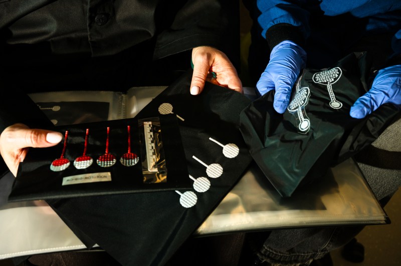 Two people wearing lab coats and gloves examine a collection of small, red and white bio-inspired models laid out on a table.