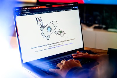 A person's hands typing on a laptop displaying a screen that shows Amazon Web Services page down.