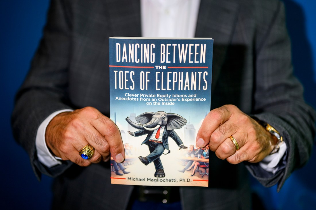 A man holds up the cover to a book titled: "Dancing Between the Toes of Elephants: Clever Private Equity Idioms and Anecdotes from an Outsider’s Experience on the Inside."