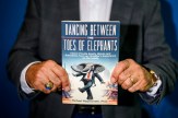 A man holds up the cover to a book titled: &quot;Dancing Between the Toes of Elephants: Clever Private Equity Idioms and Anecdotes from an Outsider’s Experience on the Inside.&quot;