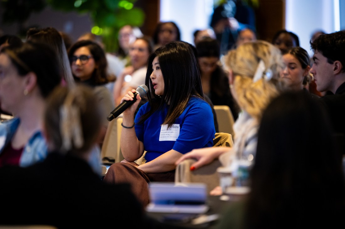 An audience member in a blue shirt holding a microphone and asking a question during a panel at the Northeastern Social Media Summit. 